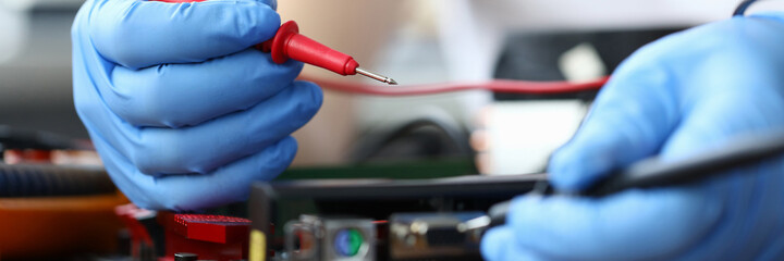 Close-up of person measuring electrical voltage. Man in protective gloves. Technician male repairing computer mainboard using digital multimeter. Technology and diy concept
