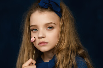 Close up Art Portrait of Beautiful young girl 10-12 years old with blonde curly long hair, posing on blue background