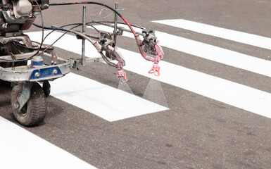 City workers paint crosswalk lanes on the road with painting machine. Close up.