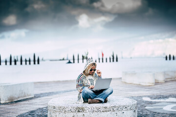 Digital nomad and technology job everywhere concept with adult young woman sit down outdoor working with laptop computer and internet roaming connection in an alternative free office under the sky