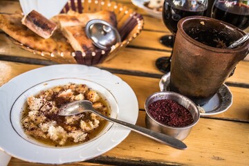 Closeup of a lunch meal - traditional Azerbaijani dish Piti soup with spices - and a clay cup with a spoon, glasses with wine, a plate with bread on the wooden table in a cafe in Shaki.
