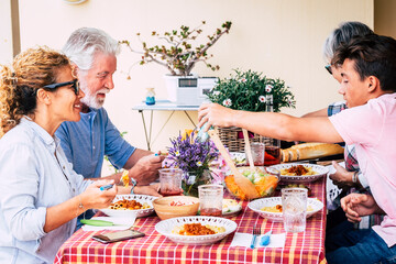 Family lunch time together with caucasian group of mixed ages people enjoy time and eat at the table - people have fun with food leisure activity - cheerful men and women various ages and years old