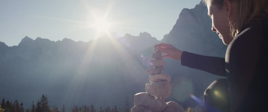 Woman put stone with hand on cairn meditation mindfulness on an autumn hiking travel in protected mountain nature in Alps close up slow motion flare beautiful sun light