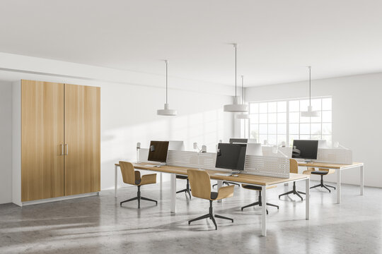 Stylish white open space office corner with wooden tables and wardrobe