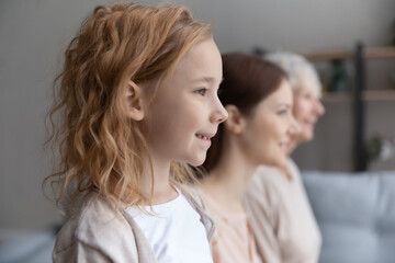Close up side view three generations of women standing in row at home, smiling pretty little girl...