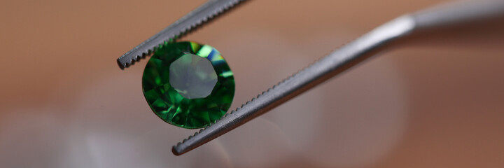 Close-up of beautiful shining crystal. Macro shot of luxury round green diamond in tweezers. Big carat size. Jeweler person checking polished brilliant. Precious stone concept