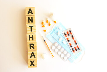 The word ANTHRAX is made of wooden cubes on a white background with medical drugs and medical mask. Medical concept.