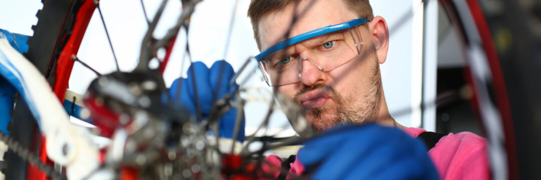 Close-up of male mechanic fixing transport. Professional handyman working with instrument repairing detail on bicycle. Worker in protective glasses and gloves. Vehicle concept