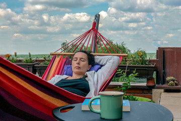 Woman lying in colorful hammock on terrace, sleeping and enjoying her free time and nice weather...