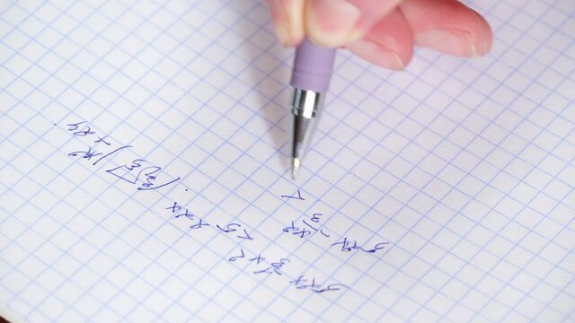 The hand holds a pen and writes a mathematical formula in a notebook. Solution of equation. The concept of education and research.
