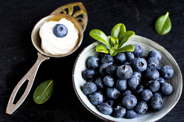 schüssel mit blaubeeren und einem löffel sahne vor schwarzen hintergrund