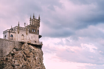 Obraz premium Swallow's nest Castle on a rock in the Black sea against the background of evening clouds, in pink tinting.