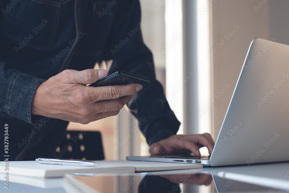 Poster multitasking business man using mobile phone surfing the internet while busy working on laptop compu