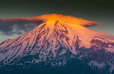 Fototapeta premium Huge snow capped Ararat Mount in the sunset in Armenia. Shining peak of the mount with orange color in clouds.