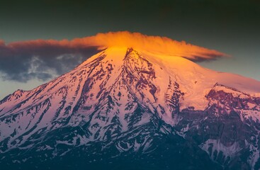 Huge snow capped Ararat Mount in the sunset in Armenia. Shining peak of the mount with orange color in clouds.