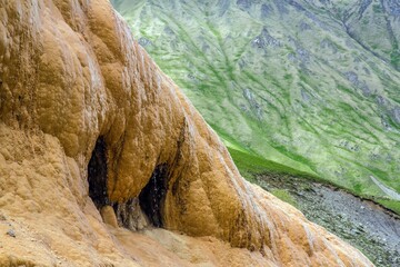 Closeup of pouring fresh water from travertine rock (tufa) in Gudauri, Georgia. Geothermal spring - unique landmark. Green hills in the background.