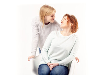 Young teenage blonde girl hugging her smiling ginger hair senior mother sitting on the chair