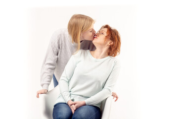 Young teenage blonde girl kissing her smiling ginger hair senior mother sitting on the chair