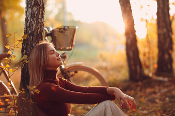 Happy active young woman sitting with vintage bicycle in autumn park at sunset