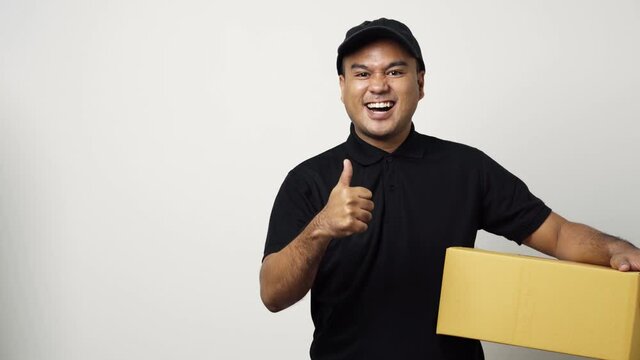Young asian delivery man in black uniform holding the parcel cardboard pointing the finger to blank space for text on isolated white background. 4k Resolution.