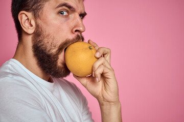 Young man with orange on a pink background in a white t-shirt emotions fun gesticulating with model...