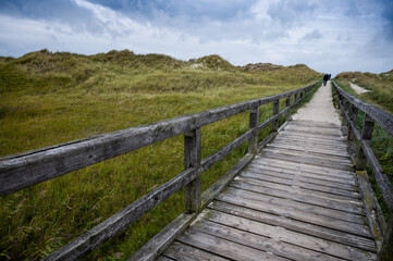 wooden jetty for direction beach through the dunes on a cloudy sky