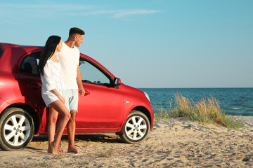 Happy couple near car on sandy beach, space for text. Summer trip