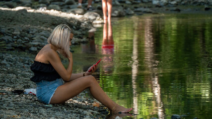 Woman sitting on river bank looking at phone