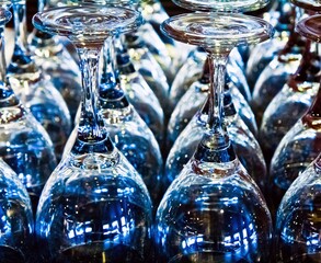 Many clean wineglasses turned upside down on the table reflecting blue and green.