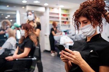 woman in hairdressing salon checking her mobile - new normal