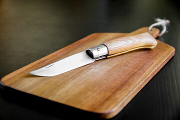 Wooden cutting board and pocket knife on a black table