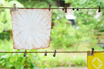 Tie dye brown and yellow color hang on clothesline with clothespin to dry for traditional fashion by natural dye art on fabric or cloth and handkerchief on nature green garden