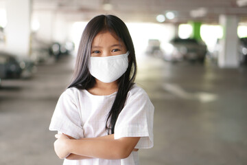 Asian child or kid girl smile wearing N95 white cloth face mask for close mouth and sick on nose with flu cough and protect PM2.5 dust by smoke or influenza covid19 and coronavirus with crossed arms