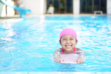Fototapeta na wymiar Asian child cute or kid girl wear swimming suit on swimming pool and smile with happy fun in water park for learn and training swim on kick board or refreshing and relax to exercise on summer holiday