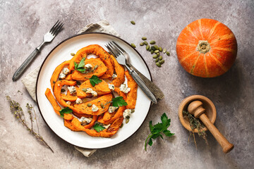 Baked pumpkin slices with herbs, seeds and cheese in a white plate on a beige rustic background. Top view, flat lay.