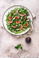 Salad figs, arugula and blue cheese in a white plate on a grunge beige background. Vegan and vegetarian lunch or dinner. Top view, flat lay, copy space.