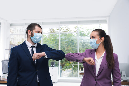 Office employees in masks greeting each other by bumping elbows at workplace