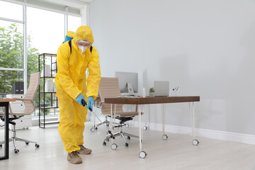 Janitor in protective suit disinfecting office to prevent spreading of COVID-19