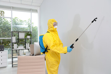 Janitor in protective suit disinfecting office to prevent spreading of COVID-19