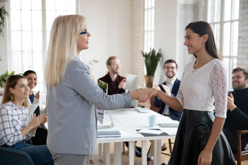 Middle-aged businesswoman shake hand of millennial female intern greeting with job employment....