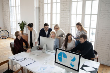 Top view of diverse multiethnic colleagues sit at desk in shared office work on computers discussing ideas. Focused coworkers busy brainstorming in coworking space, use PC cooperate in groups.