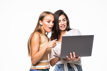 Portrait of two cheerful women looking at the laptop isolated over white background.