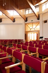 Interior of a modern church hall with red seats and bright windows