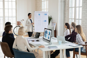 Young indian female speaker or coach stand make flip chart presentation for diverse employees in...