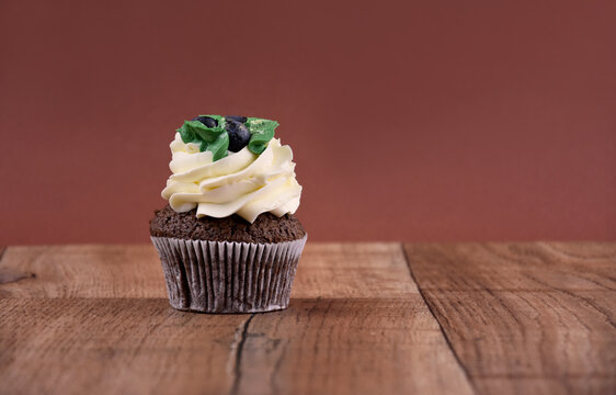 Chocolate cupcake with vanilla frosting on a wooden background stock images. Cupcake on the table. Delicious cupcake brown frame stock images. Chocolate cupcake brown border with copy space for text