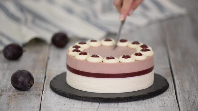 Cutting delicious plum mousse cake with whipped cream.