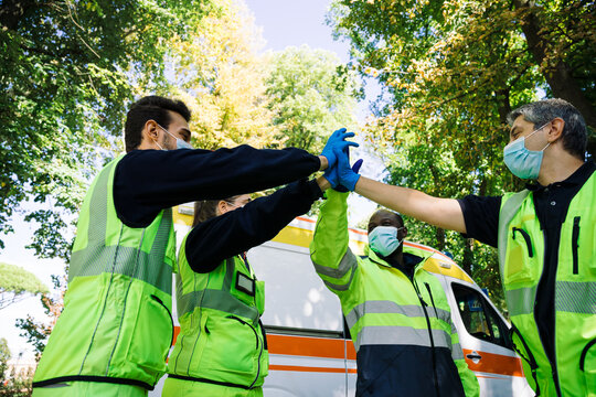 Group of first aid personnel with ambulance high-five with their hands as a sign of success after an emergency call during the Coronavirus pandemic, Covid-19 - Concept of teamwork and union