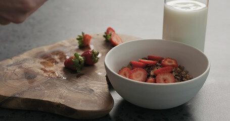 closeup man hands slicing fresh strawberries into chocolate granola