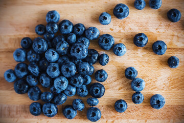 Top view of a wooden kitchen board, on which lies a handful of ripe washed large delicious blueberries, ready to eat. Harvest of berries.