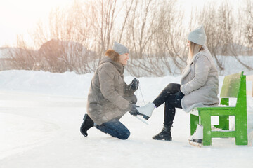 Fototapeta na wymiar Man helps to put on skates for ice rink snow to girl, concept of winter vacation, family rest